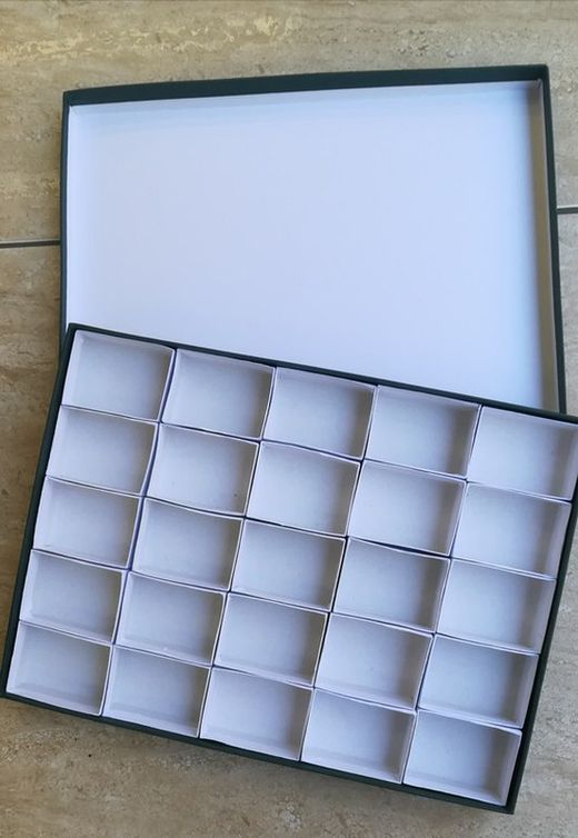Estuche verde de cartón con 25 compartimentos interiores de 40x60 mm.